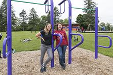 Two women leaning against park equipment at a park with swings and bikes in the background